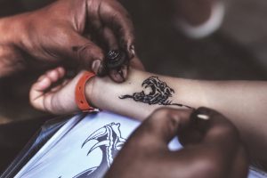 Close-up shot of a child getting a henna tattoo on their arm.
