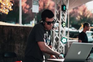 DJ performing outdoors in Fayetteville, AR using a laptop and headphones.