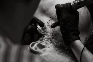 A tattoo artist skillfully inks a floral design on a man's neck, showcasing detailed craftsmanship.