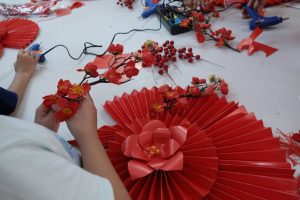 Hands crafting with red paper flowers and decor, showcasing creativity and art skills.