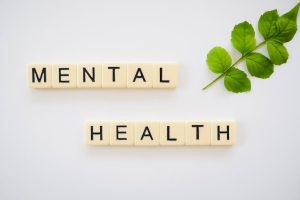 Scrabble tiles spelling 'Mental Health' with green leaves on a white background.