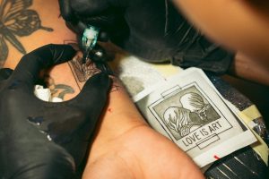 Detailed view of a tattoo artist inking a 'Love is Art' design onto skin, emphasizing precision and creativity.
