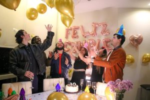 Group of friends celebrating a birthday indoors with balloons and cake.