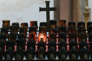 Dimly lit church interior with glowing votive candles and a cross.