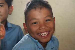 Close-up of a smiling child in a blue shirt, indoors, conveying joy and warmth.