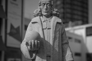 Black and white photo of a historical stone statue in a modern cityscape.