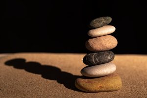 A stack of balanced pebbles on sand against a dark background symbolizing balance and harmony.