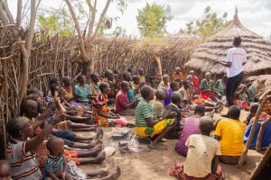 A gathering of people in traditional African village, sitting and interacting outdoors.