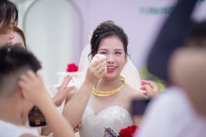 A joyful bride in Hanoi wipes away tears of happiness on her wedding day, surrounded by friends.
