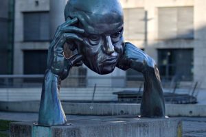 Bronze head sculpture of a man resting on his arms, displayed outdoors.