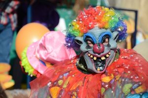 Vibrant clown with rainbow wig and mask at a lively outdoor carnival parade.