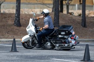 Police officer on a motorcycle practicing maneuvers between traffic cones outdoors.
