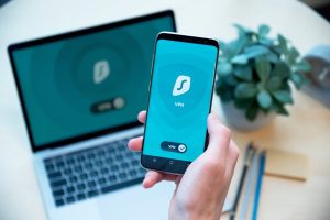 Close-up of a hand holding a smartphone with VPN app, laptop in the background, showcasing digital security.