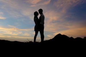 A romantic silhouette of a couple standing face to face against a stunning sunset backdrop.