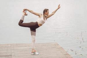 A woman stretches in a yoga pose on a wooden pier by a serene lake, showcasing flexibility and balance.