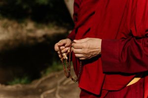 A monk dressed in traditional robes holding prayer beads outdoors, symbolizing spirituality.