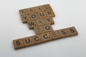 Wooden tiles spell 'Fail Your Way to Success' emphasizing perseverance.