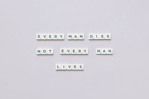 Scrabble tiles spelling 'Every man dies, not every man lives' on gray background.