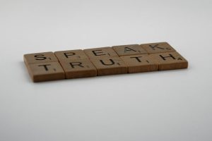 Wooden Scrabble tiles forming the phrase 'Speak Truth' on a white surface.