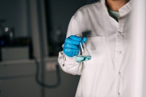 Scientist in white coat holding a flask with blue liquid in a laboratory, showcasing scientific research.