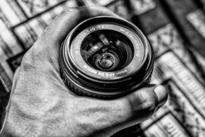 Black and white image of a Nikon camera lens being held, showcasing classic photography equipment.