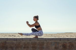 Side view of a woman balancing in a yoga pose on a beach wall, promoting a healthy lifestyle.