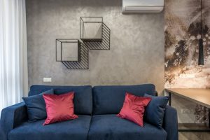 Comfortable soft sofa with pillows placed in modern living room near wall with creative geometric shelves