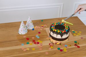Hand slicing a chocolate cake with lively candy decorations at a festive party setting.