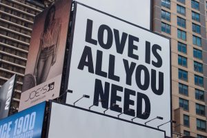 Large city billboard reads 'Love Is All You Need' in New York City street.