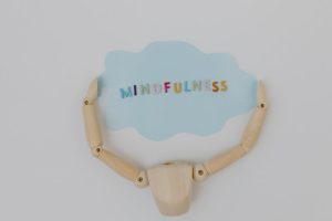 Wooden mannequin arms holding a blue cloud with 'Mindfulness' text, promoting self-awareness.
