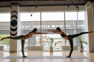 Two women performing yoga poses in a contemporary indoor studio.