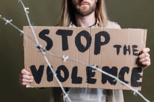 Close-up of a protester holding a cardboard sign reading 'Stop the Violence' with barb wire in focus.