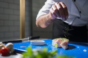 A chef skillfully seasons a gourmet dish in a modern kitchen, highlighting culinary expertise.