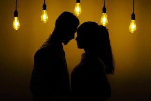 A romantic silhouette of a couple under hanging bulbs, highlighting intimacy and connection.