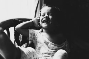 Smiling child in black and white, capturing carefree joy near a sunny window.