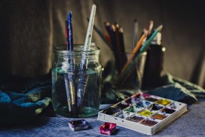 A creative still life of paintbrushes in a jar with watercolors and pencils, perfect for artistic inspiration.