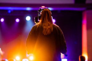 Woman wearing headphones at a concert with vibrant stage lights and colors.